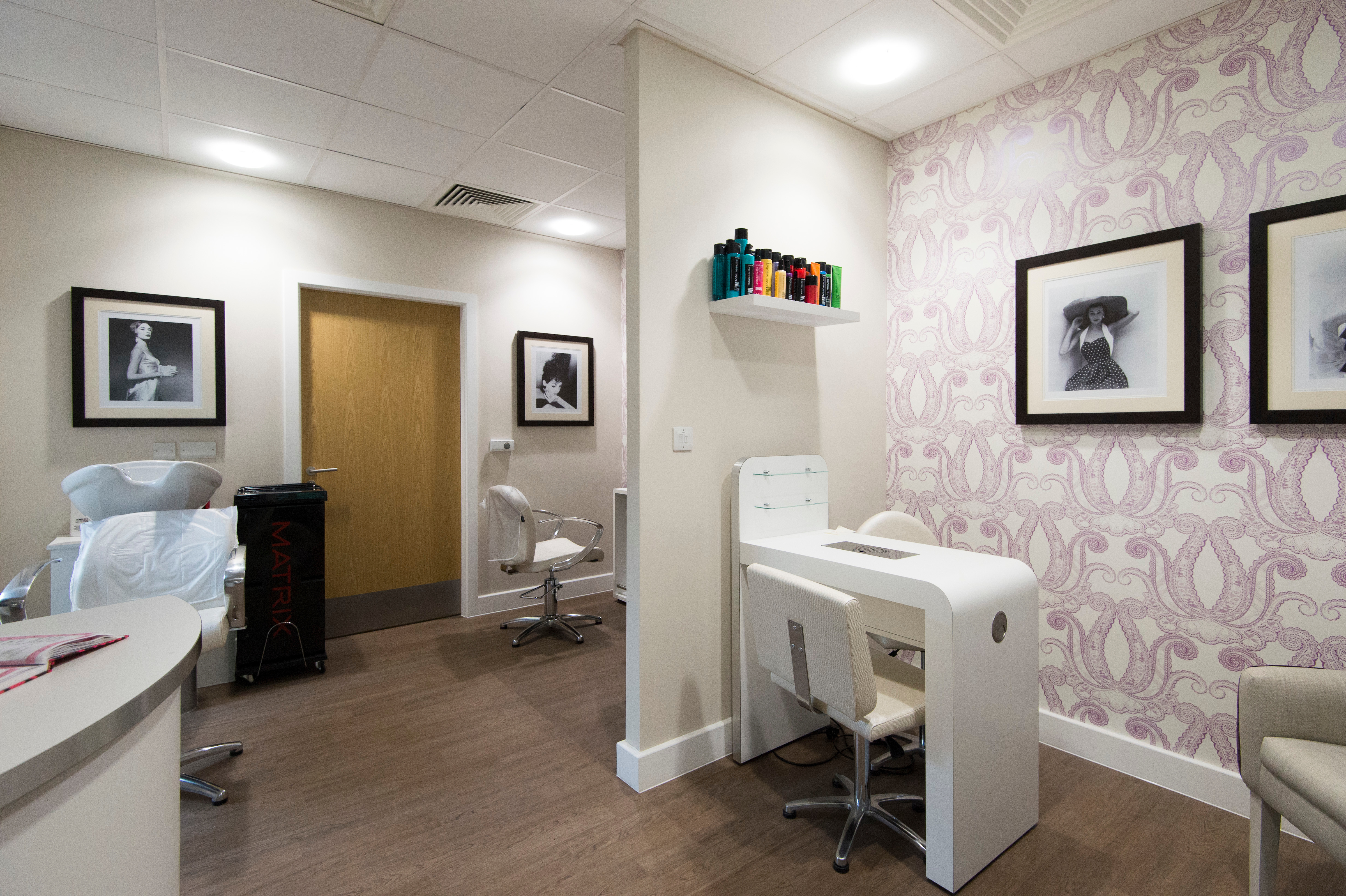 Beauty and hair salon room with sink, styling chair, manicure table and shelves stocked with hair products.
