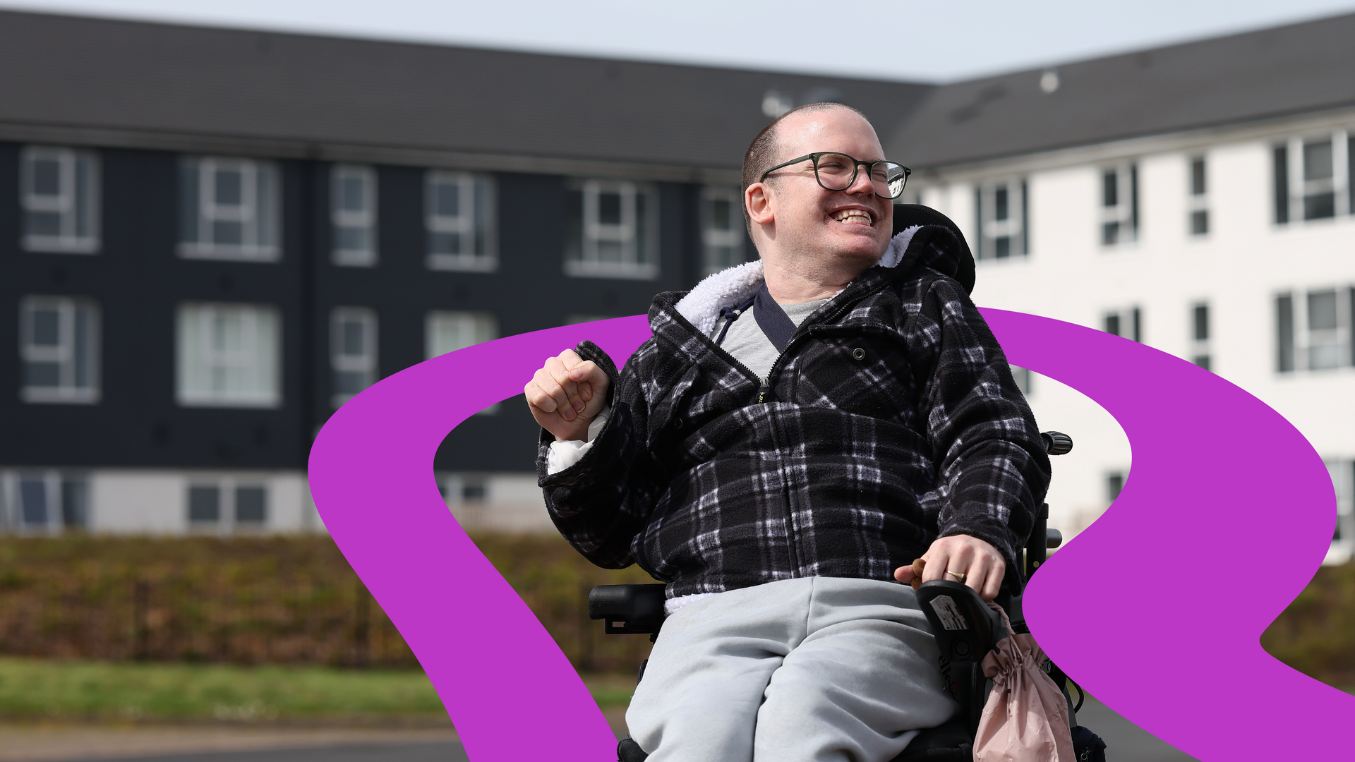 A Riverside resident using a powered wheelchair outside a modern residential building
