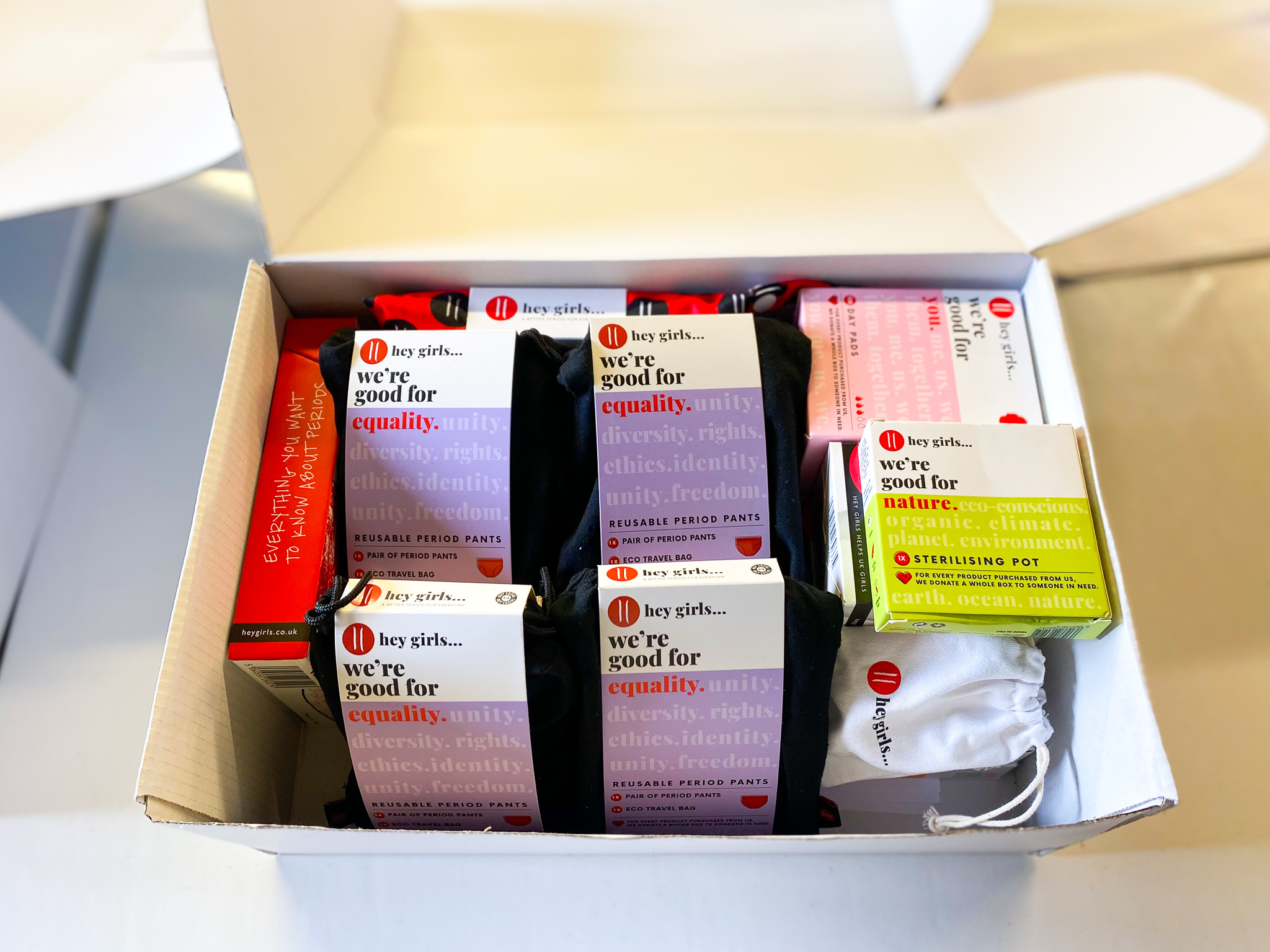 Open box containing Hey Girls reusable period products and menstrual health items packaged for distribution.
