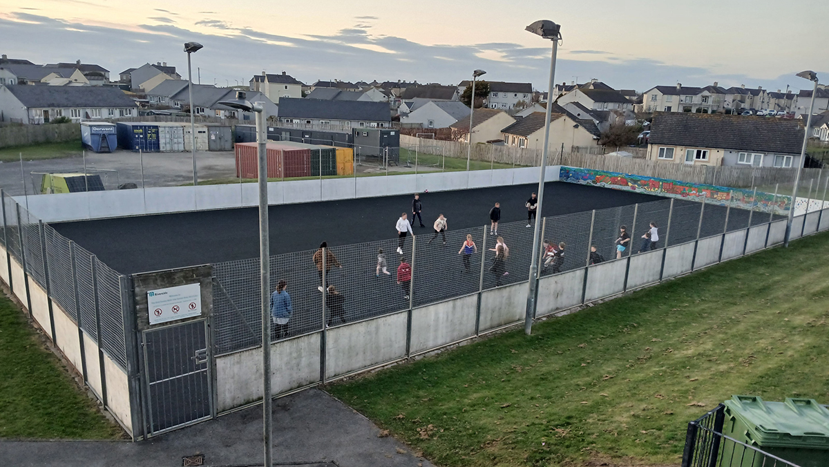 Young people taking part in an outdoor sports session on a fenced MUGA pitch in a residential neighbourhood.