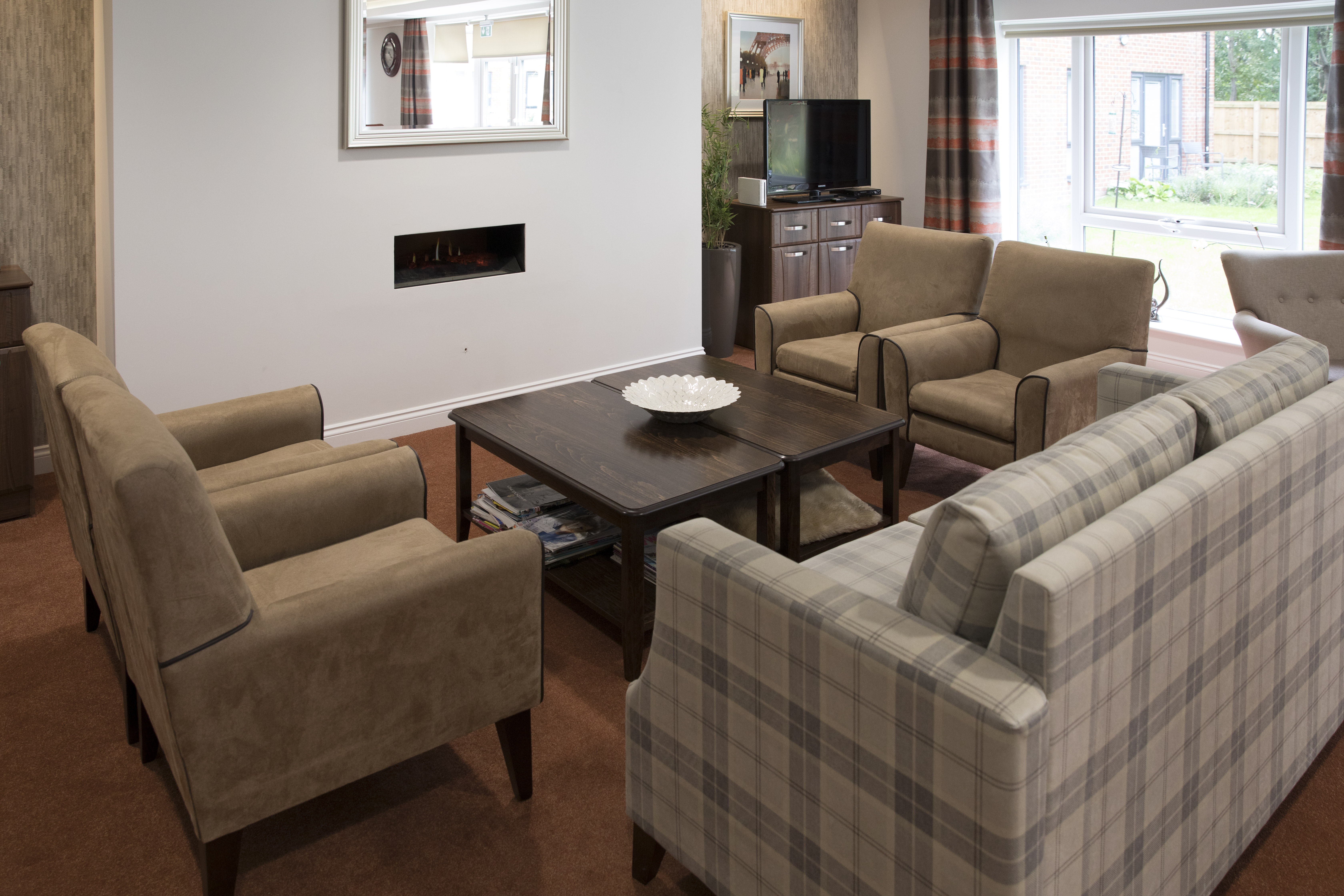 Cosy lounge area with armchairs and sofa around a coffee table, featuring a wall‑mounted fireplace and television.