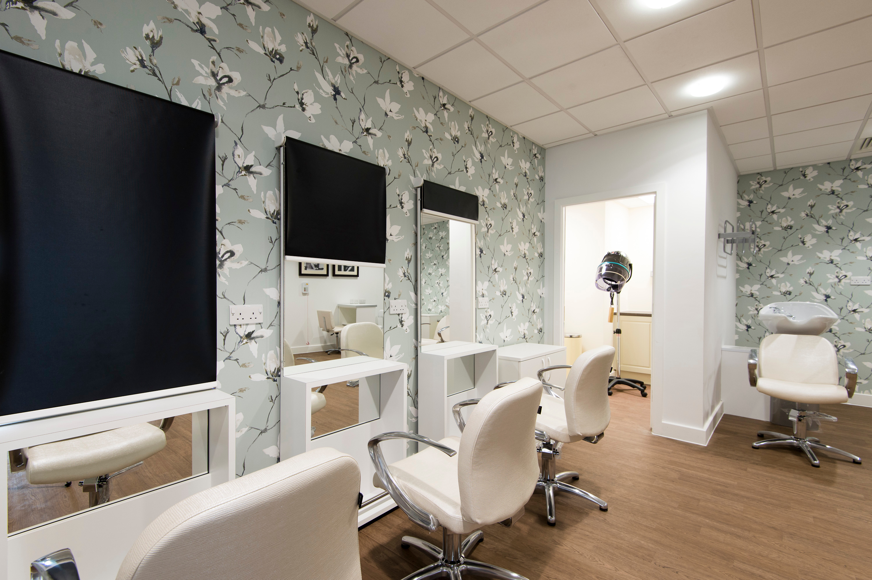 On‑site hair salon with styling chairs, mirrors, hairdryer hood and wash basin, decorated with floral wall patterns.