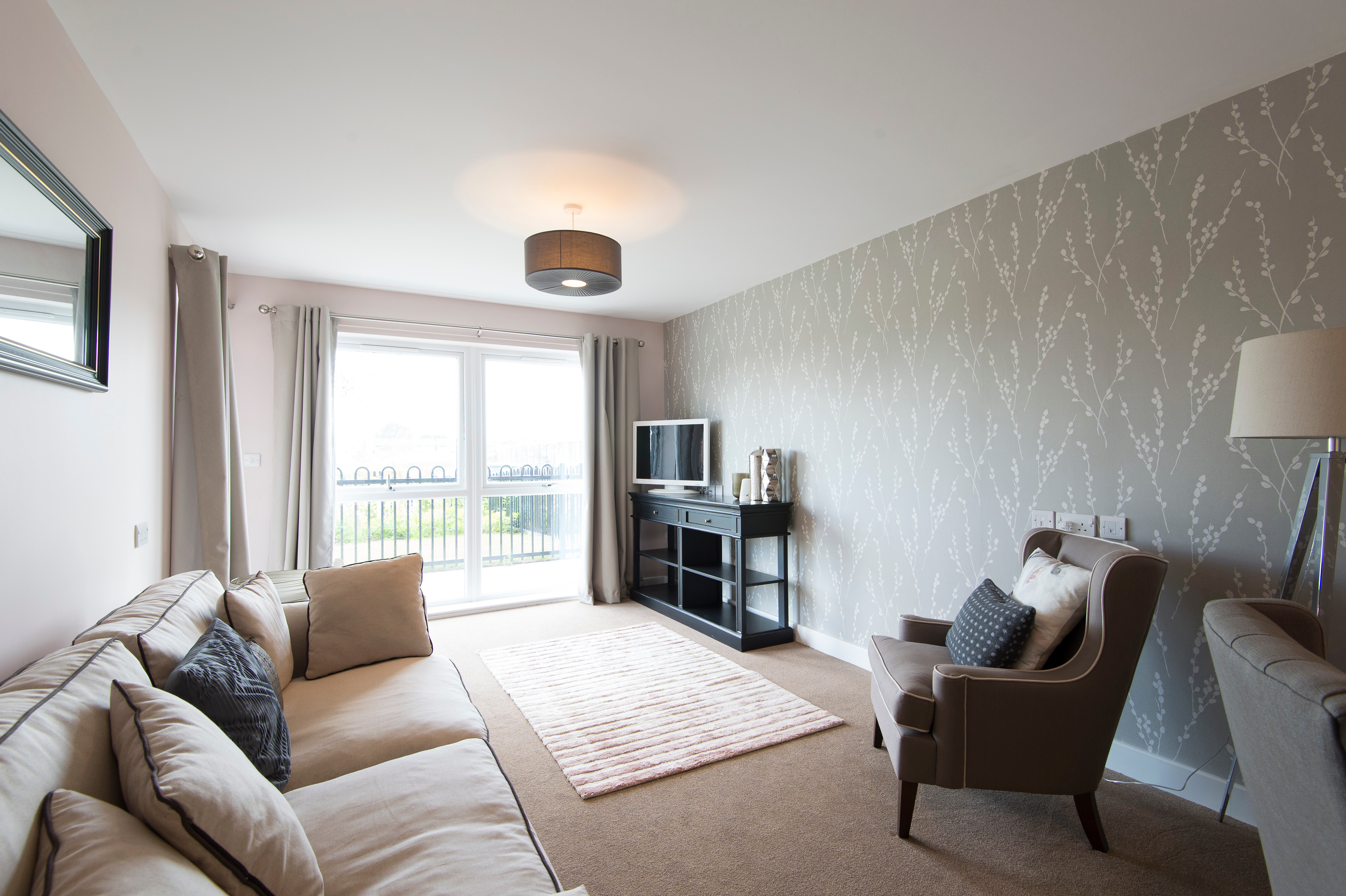 Comfortable living room with sofa, armchair and TV unit, featuring large windows and soft neutral décor.