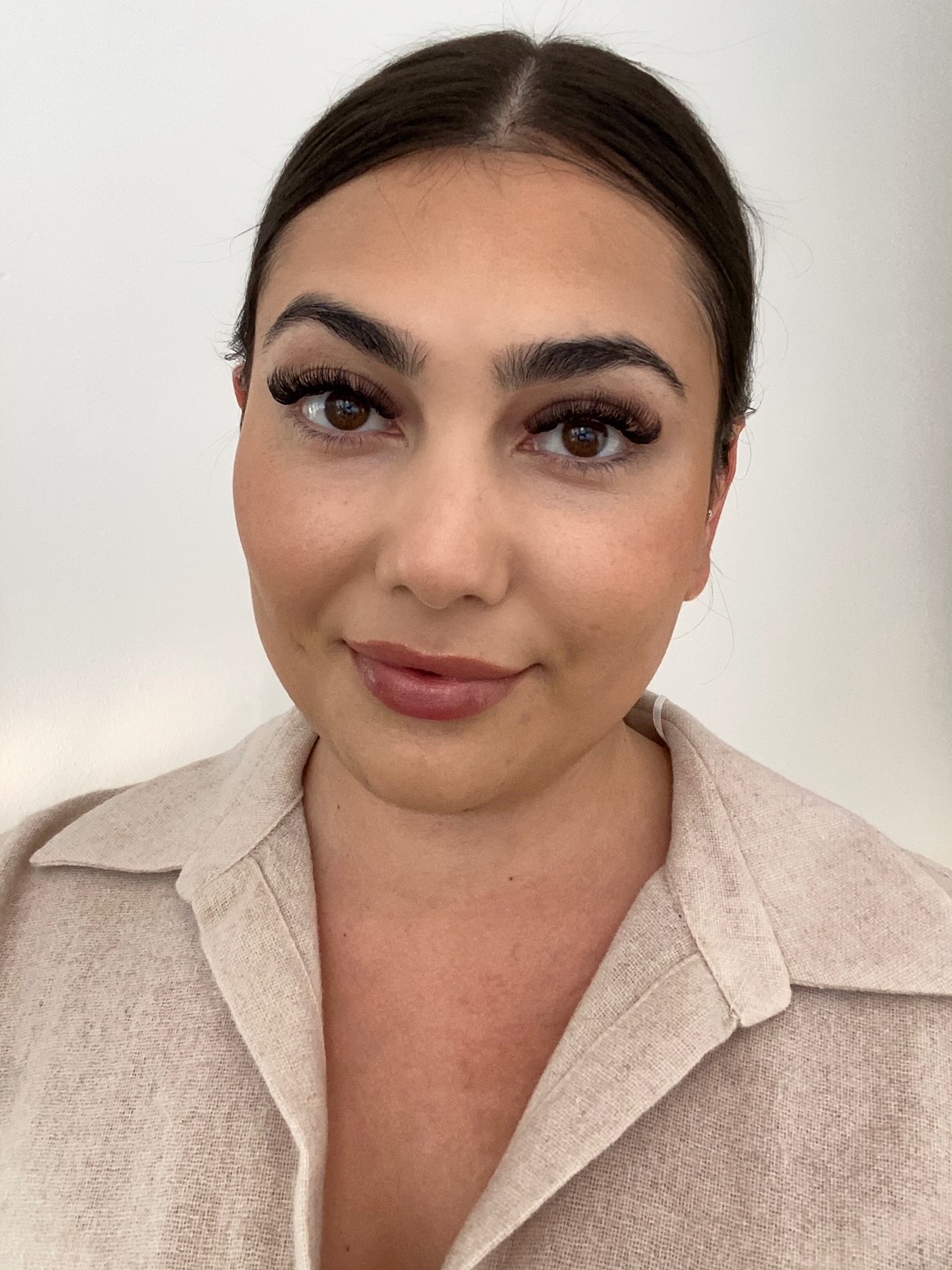 Portrait of a person facing the camera against a plain light background. They are wearing a light‑coloured collared top, with dark hair pulled back, and even lighting highlighting the face and shoulders.