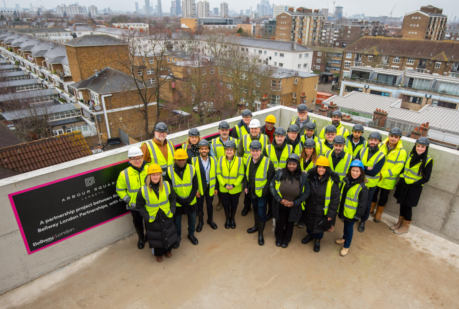 Large group of construction staff in high‑visibility clothing gathered on a rooftop at the Arbour Square development in Lambeth.