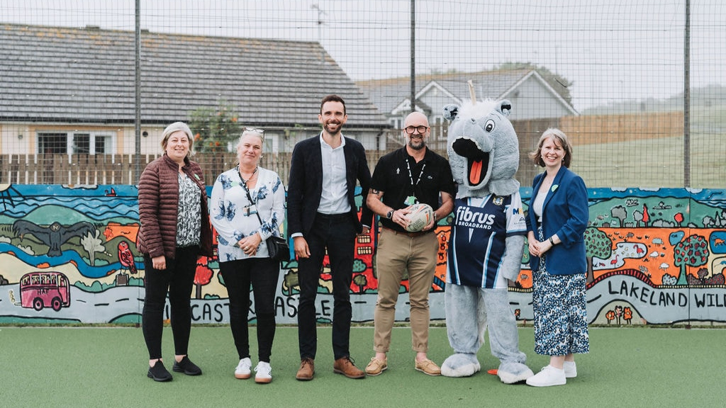 Community partners and a sports mascot standing together in front of a colourful mural during a Riverside neighbourhood engagement event.