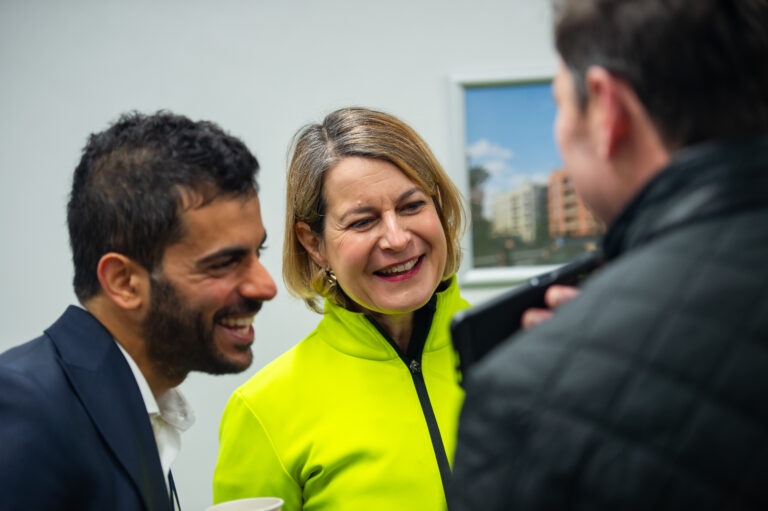Team members holding a discussion indoors beside a wall display featuring building imagery.