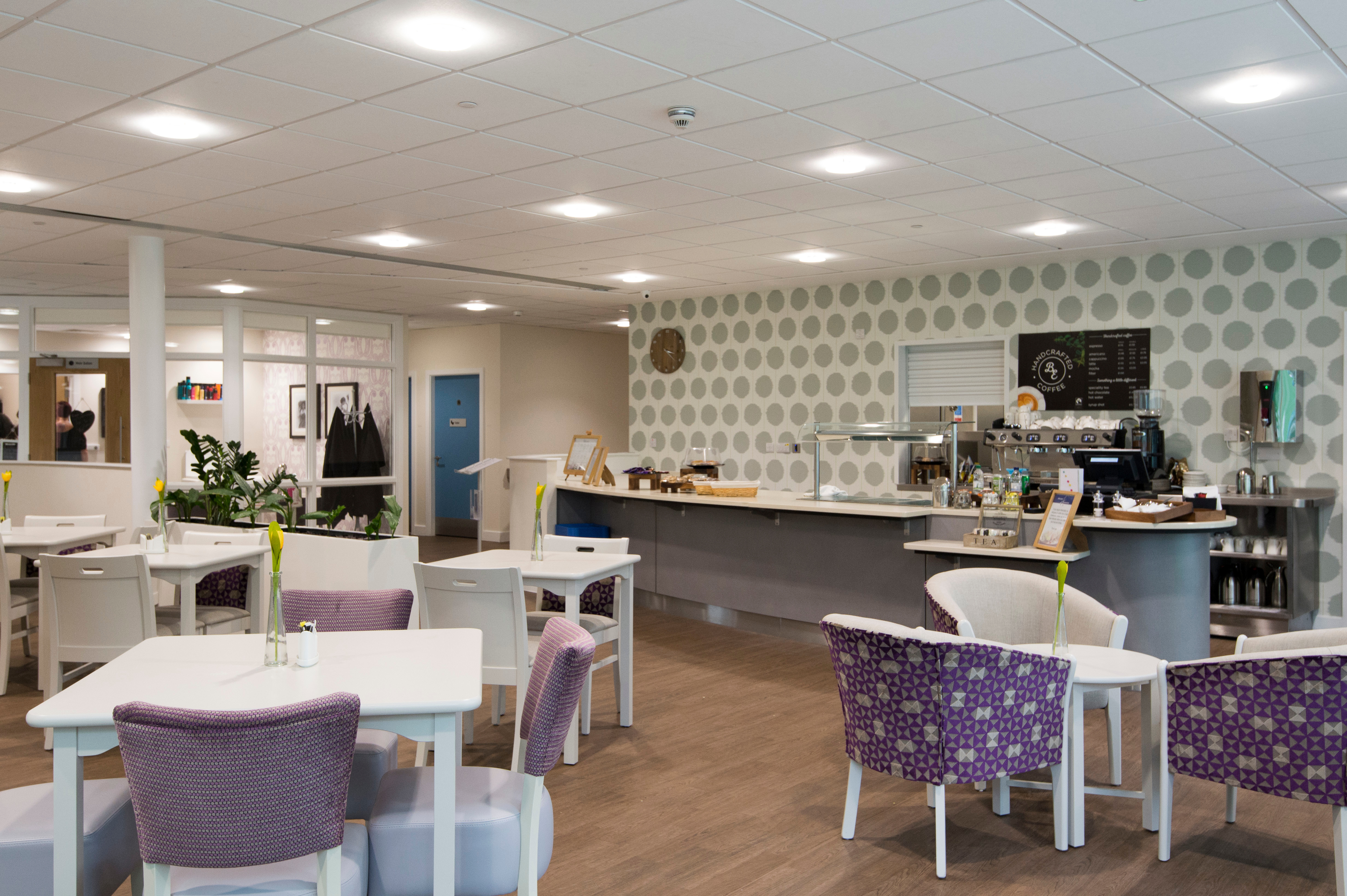 Dining area with tables and chairs next to a coffee bar serving drinks and snacks in a communal space.