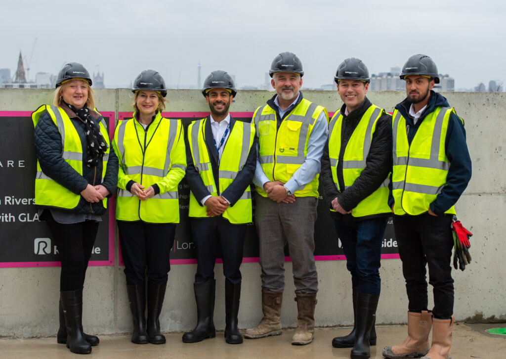 Construction team wearing safety gear standing together in front of Arbour Square project signage.