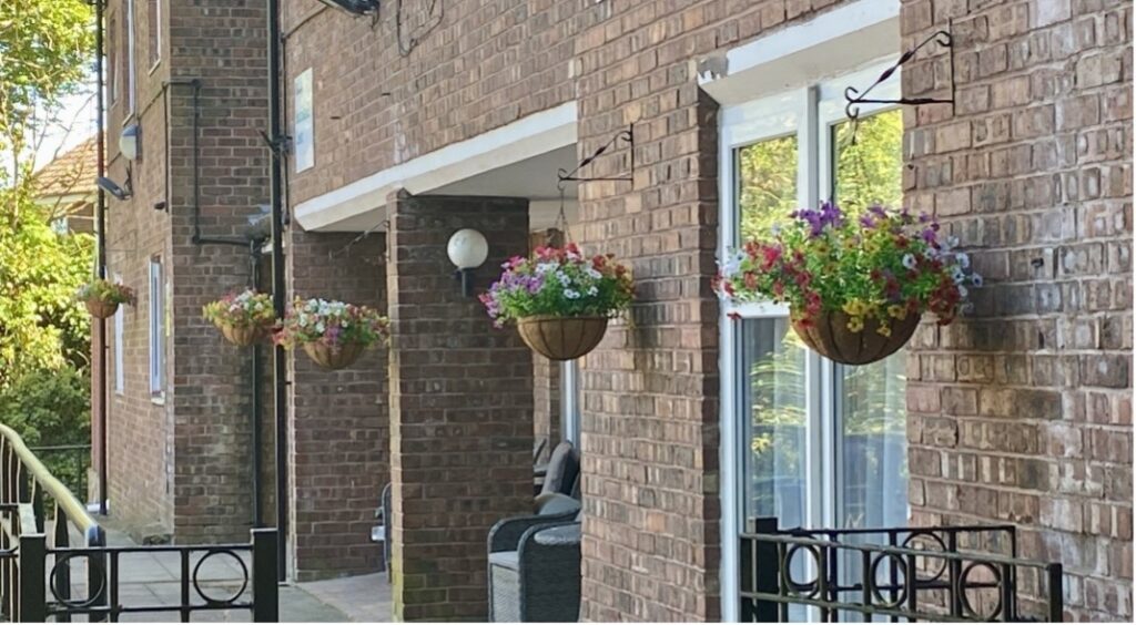 Five baskets filled with colourful flowers hang outside of apartments in Southlands Court.