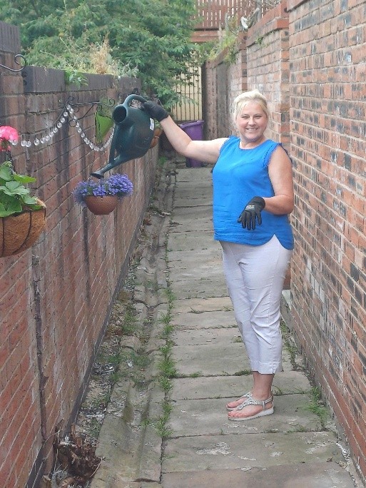 Woman in a blue top waters hanging baskets filled with colourful flowers